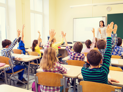 A class of students raises their hands in front of their teacher.