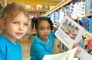 Two girls face the camera holding books.