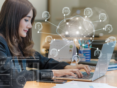 A woman looks at a laptop. An image of a brain connected to technology icons is imposed over the image.