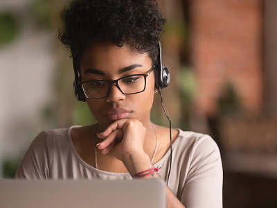A black teenage girl wears headphones and looks at a screen.