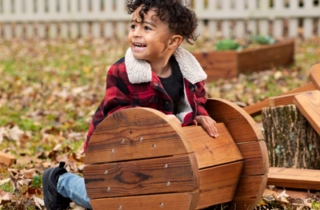 A boy in a red plaid jacket leans on an outdoor toy.