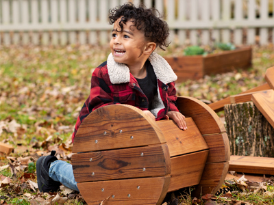 A boy in a red plaid jacket leans on an outdoor toy.