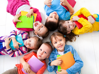 A circle of kids lays together wearing colorful clothes and clutching photos.