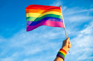 Colorful rainbow gay pride flag being waved in the breeze by a hand wearing a rainbow sweatband