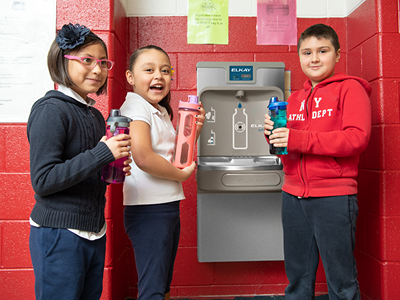 Three students stand beside a filtered water fountain, holding reusable water bottles.