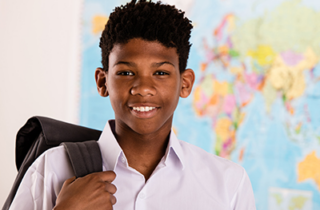 A black teenager holds a backpack and stands in front of a world map.
