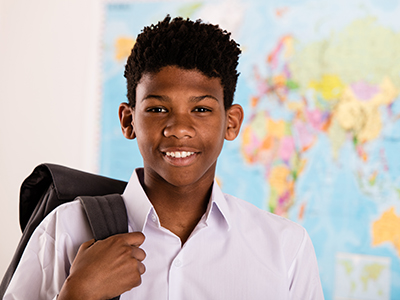A black teenager holds a backpack and stands in front of a world map.