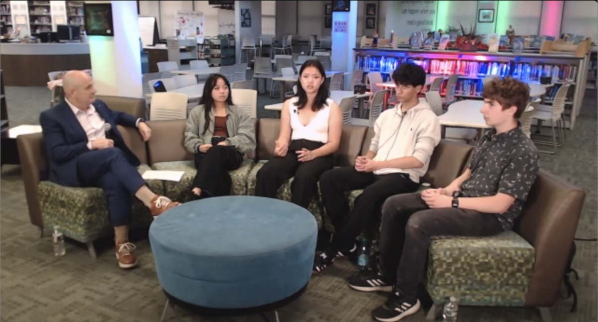 A panel of students sitting around a table talking with a teacher